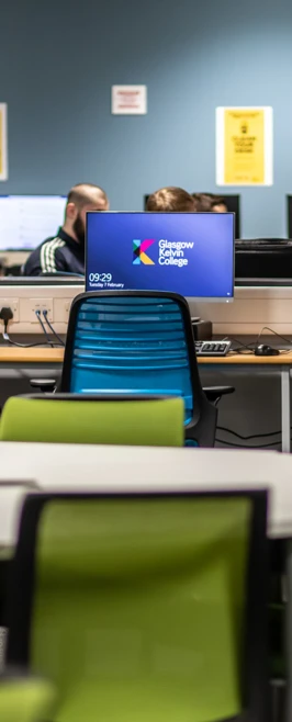 Computer area in the Glasgow Kelvin College Easterhouse library with blue chairs, desktop monitors, and green classroom seating in the foreground. Computer area in the Glasgow Kelvin College Easterhouse library with blue chairs, desktop monitors, and green classroom seating in the foreground.